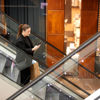 A woman holding a phone in her hand while riding an escalator, with a brown paper bag in her left hand.