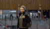A young woman standing in a shopping centre stares directly into the camera.